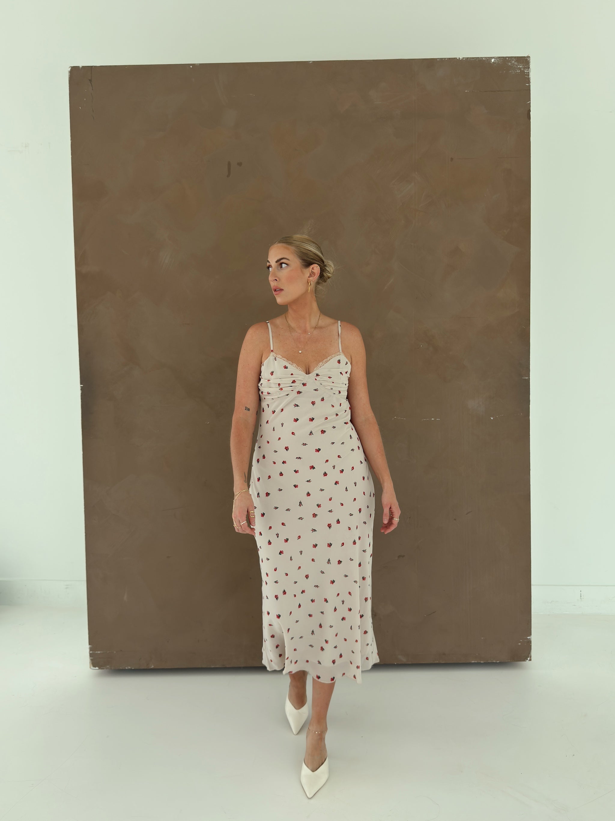 A model wearing a beige spaghetti-strap slip dress with small red ditsy floral print and lace trim.
