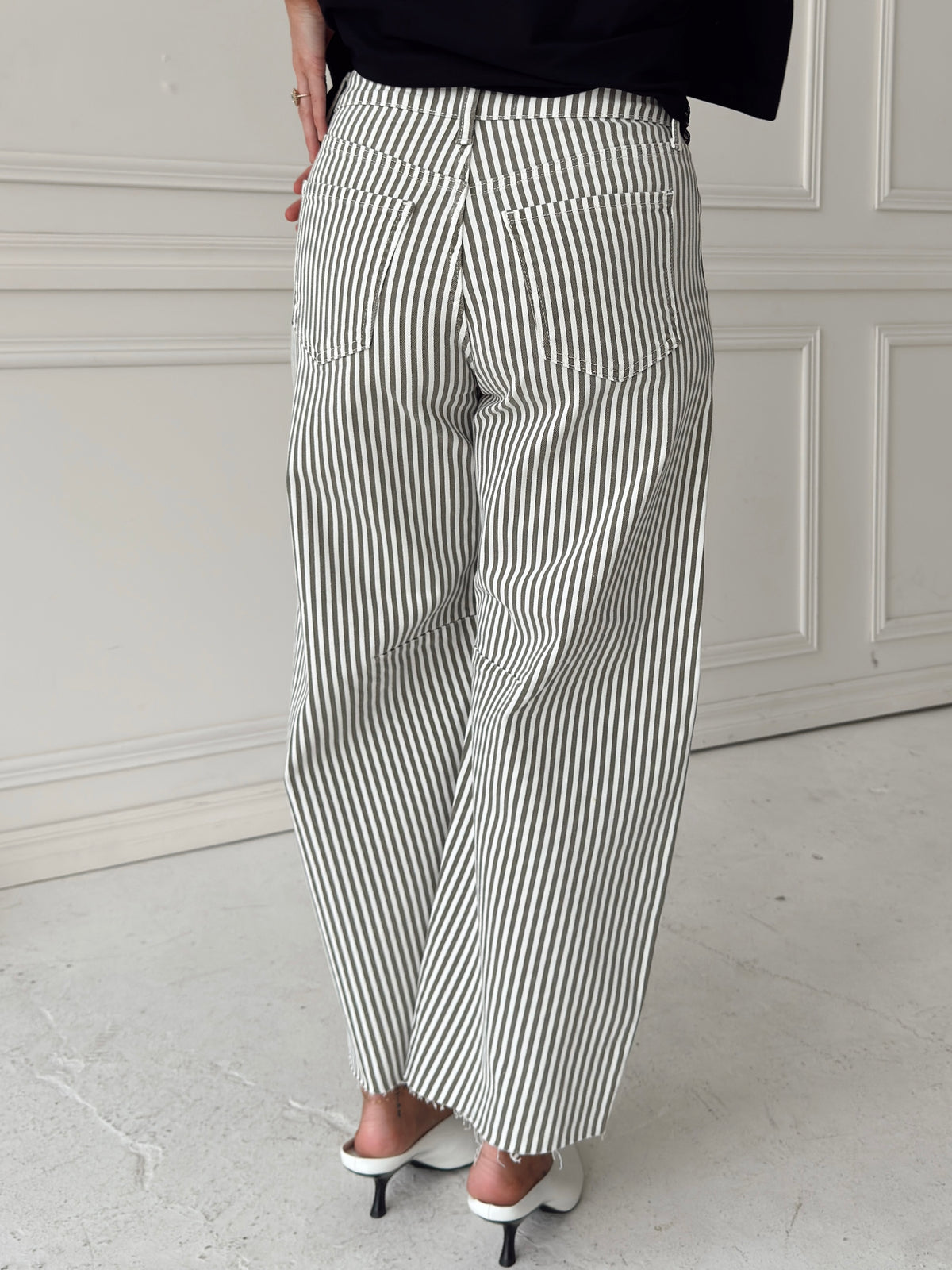 A woman waist down modeling a pair of wide-leg barrel jeans with thin olive and white vertical stripes, paired with a black t-shirt.