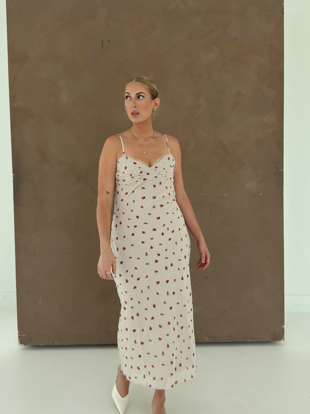 A model wearing a beige spaghetti-strap slip dress with small red ditsy floral print and lace trim.