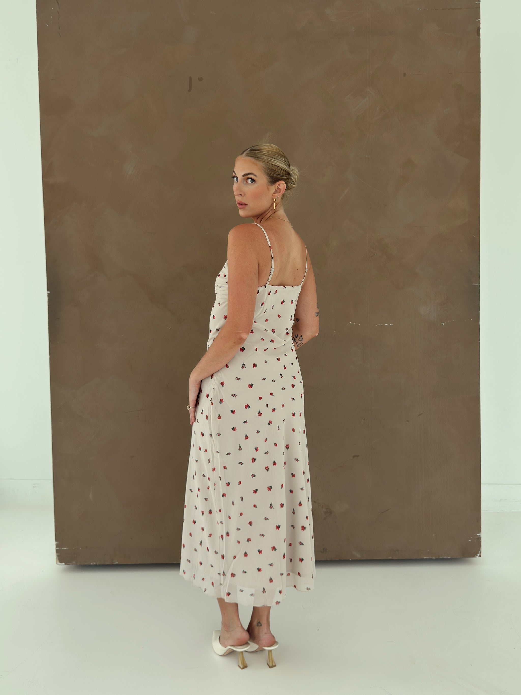 A model wearing a beige spaghetti-strap slip dress with small red ditsy floral print and lace trim.