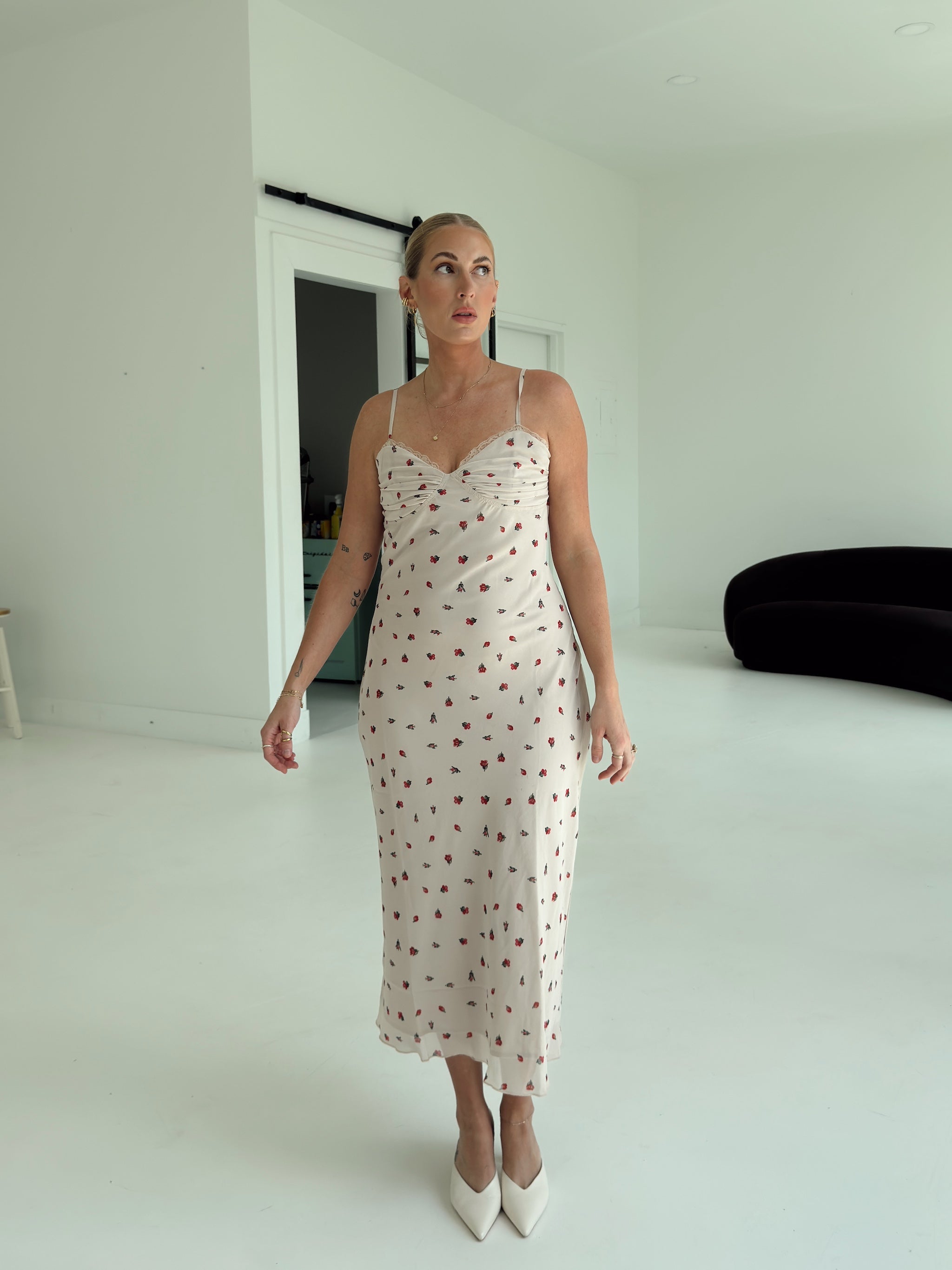 A model wearing a beige spaghetti-strap slip dress with small red ditsy floral print and lace trim.