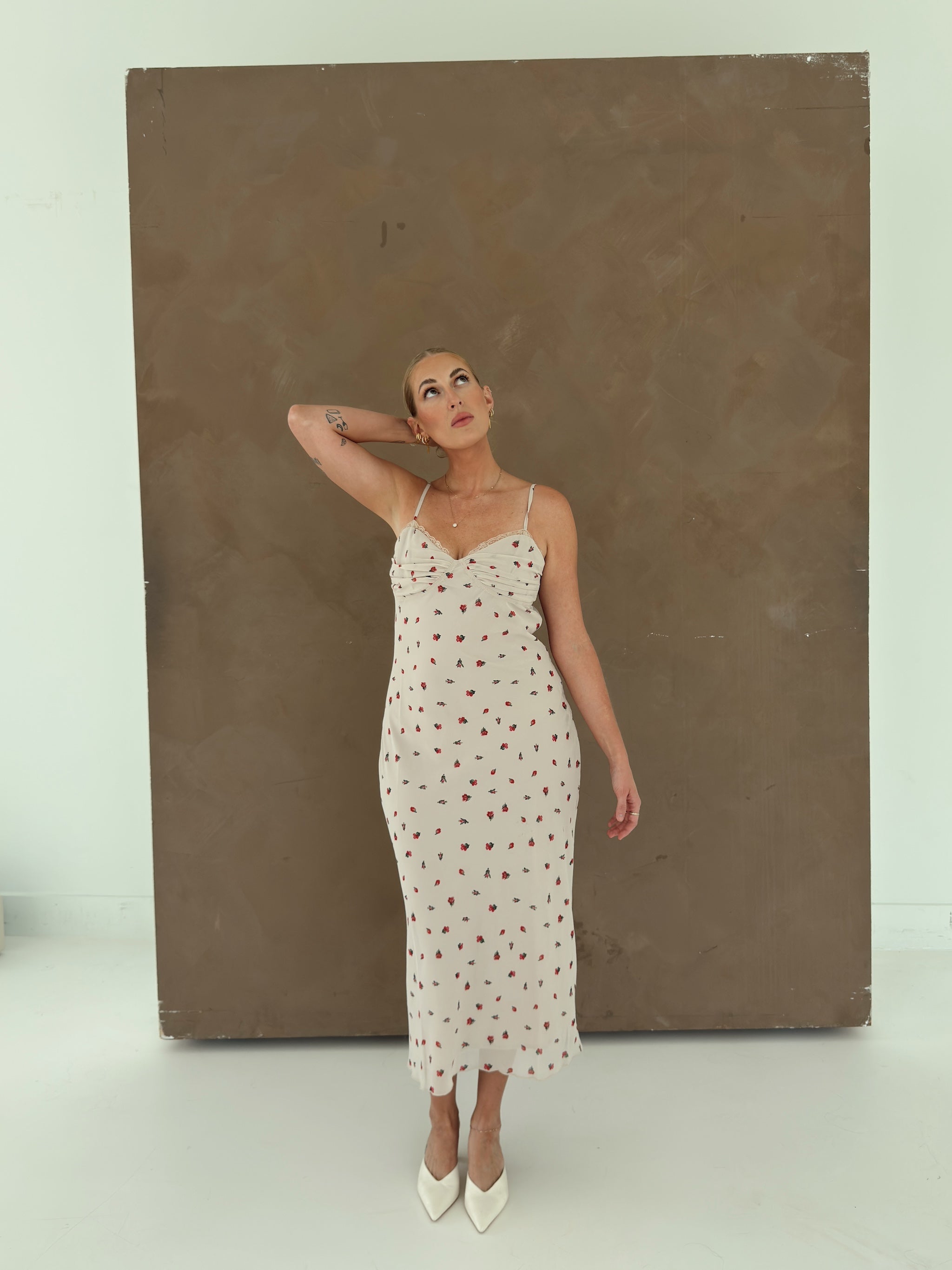 A model wearing a beige spaghetti-strap slip dress with small red ditsy floral print and lace trim.