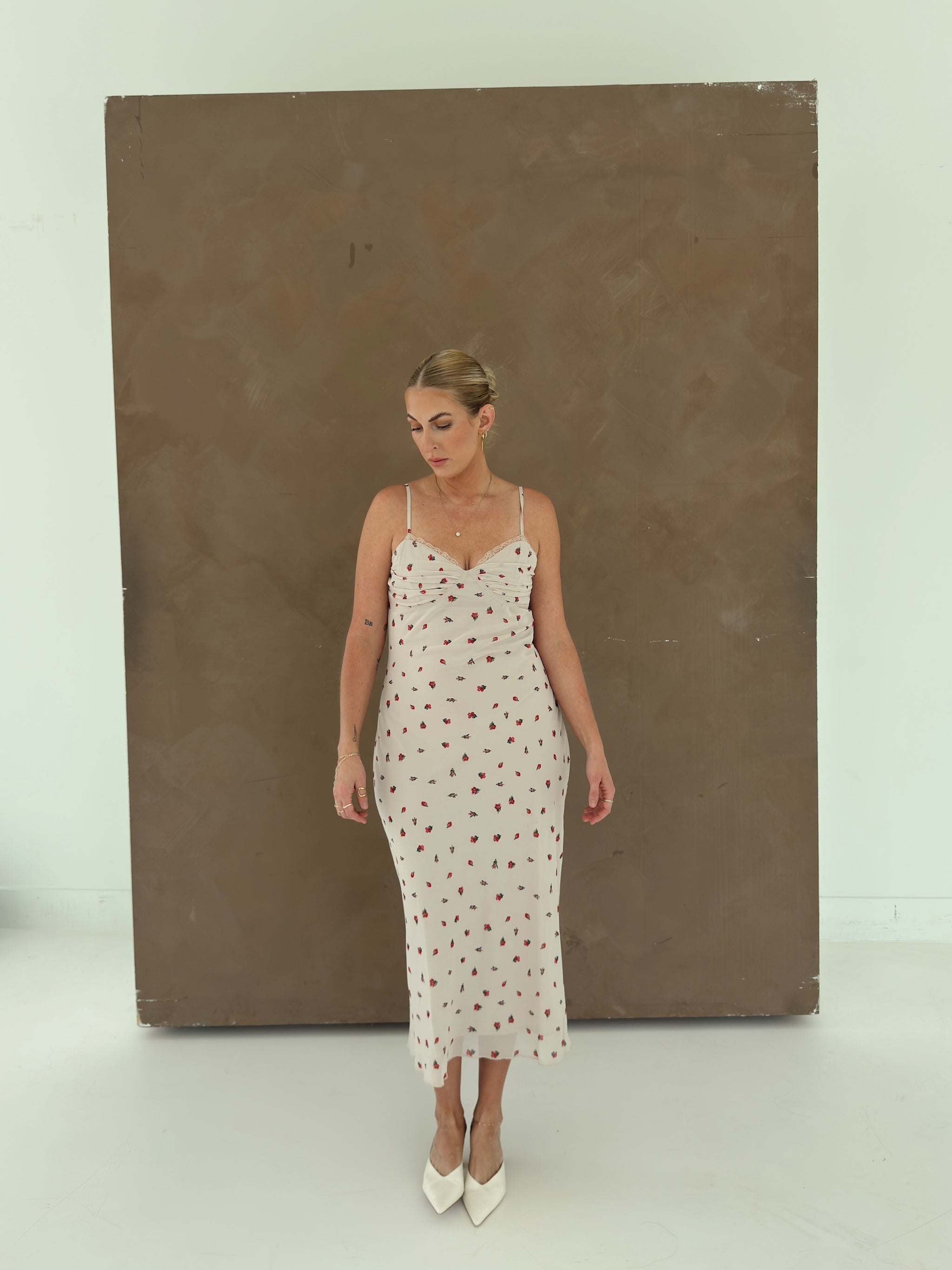 A model wearing a beige spaghetti-strap slip dress with small red ditsy floral print and lace trim.