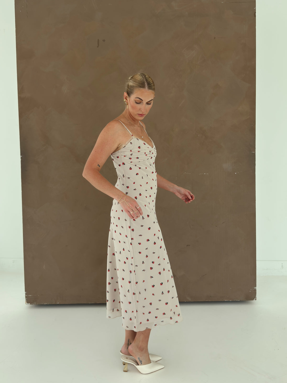 A model wearing a beige spaghetti-strap slip dress with small red ditsy floral print and lace trim.