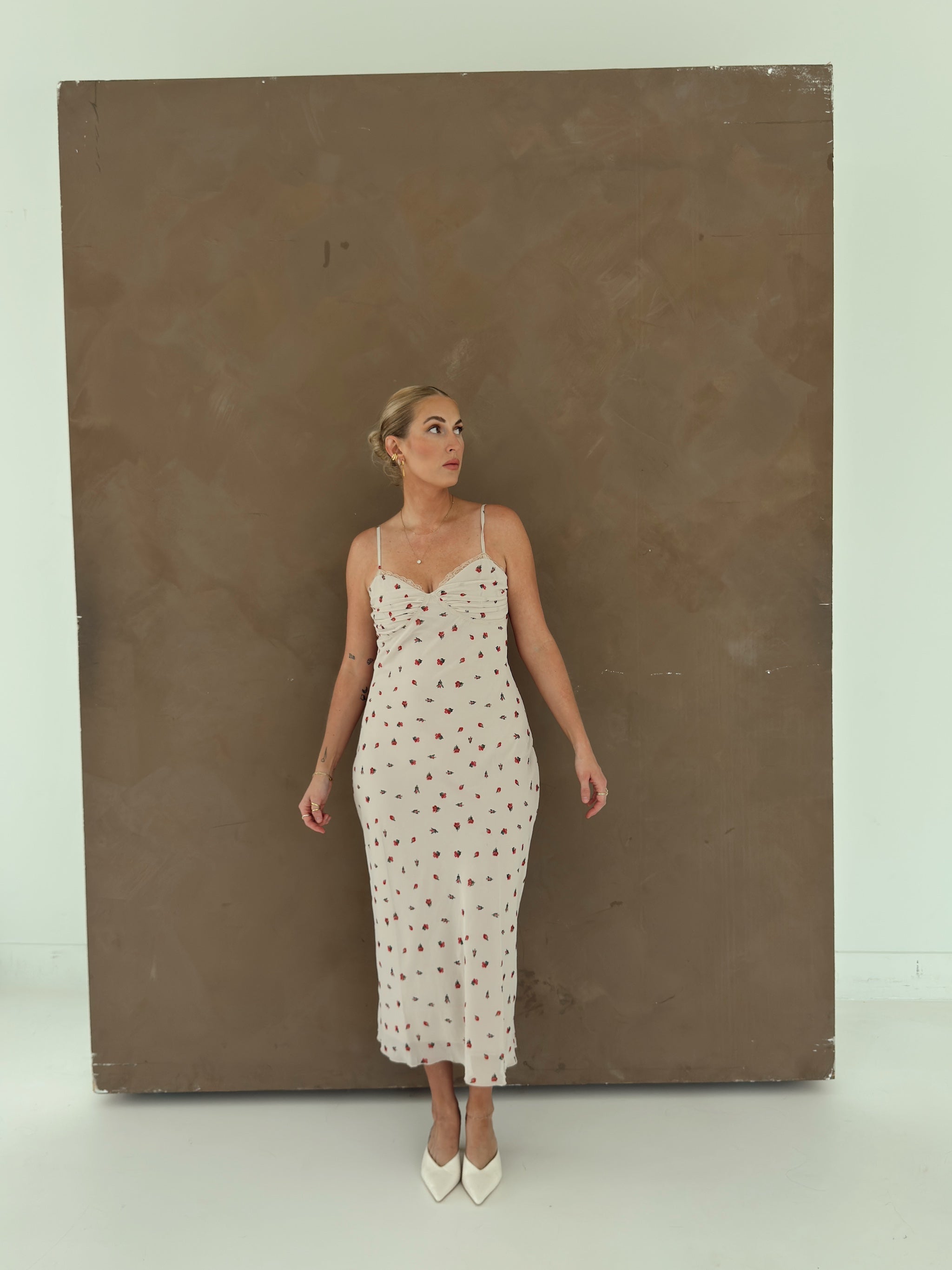 A model wearing a beige spaghetti-strap slip dress with small red ditsy floral print and lace trim.