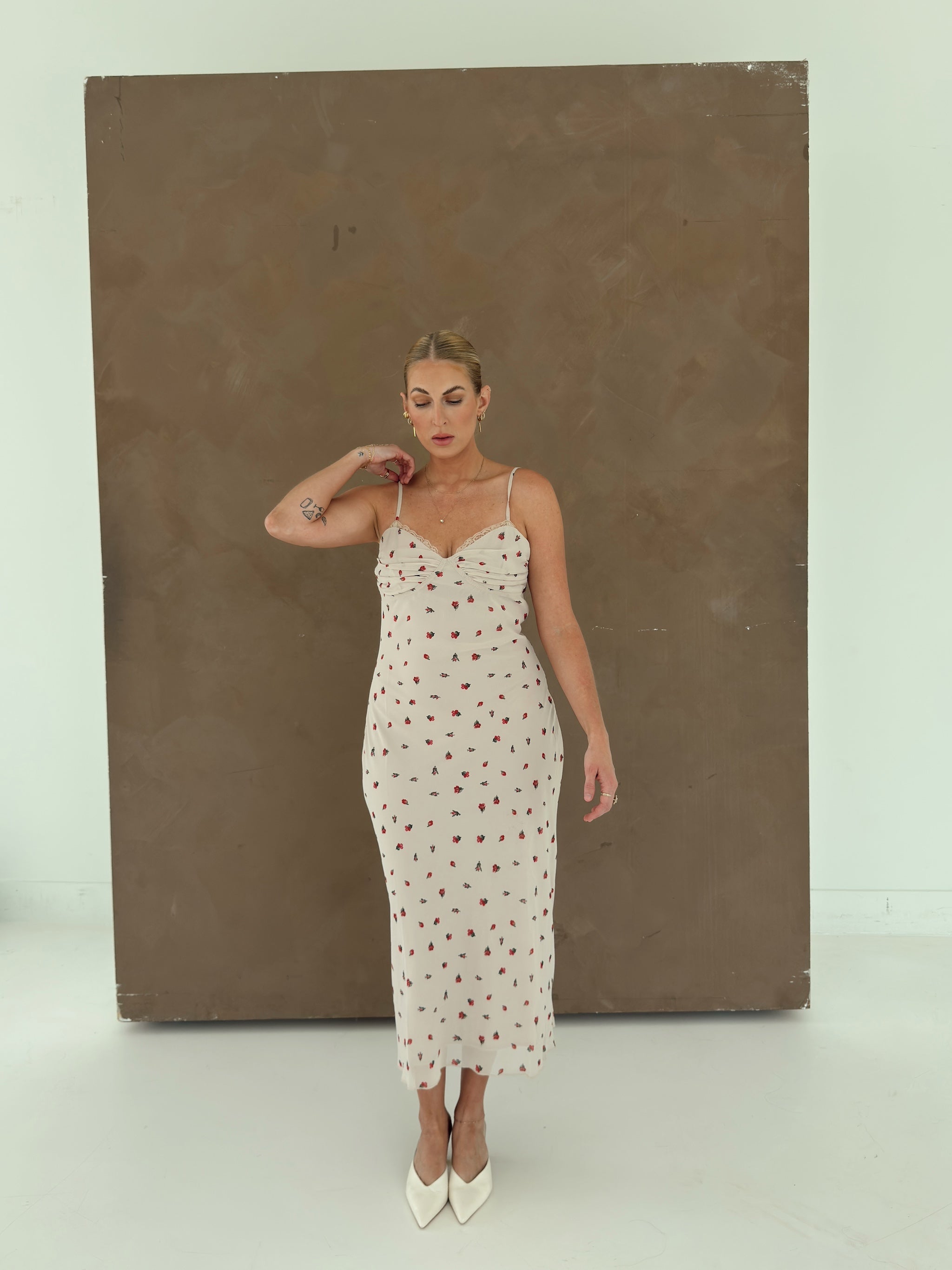 A model wearing a beige spaghetti-strap slip dress with small red ditsy floral print and lace trim.