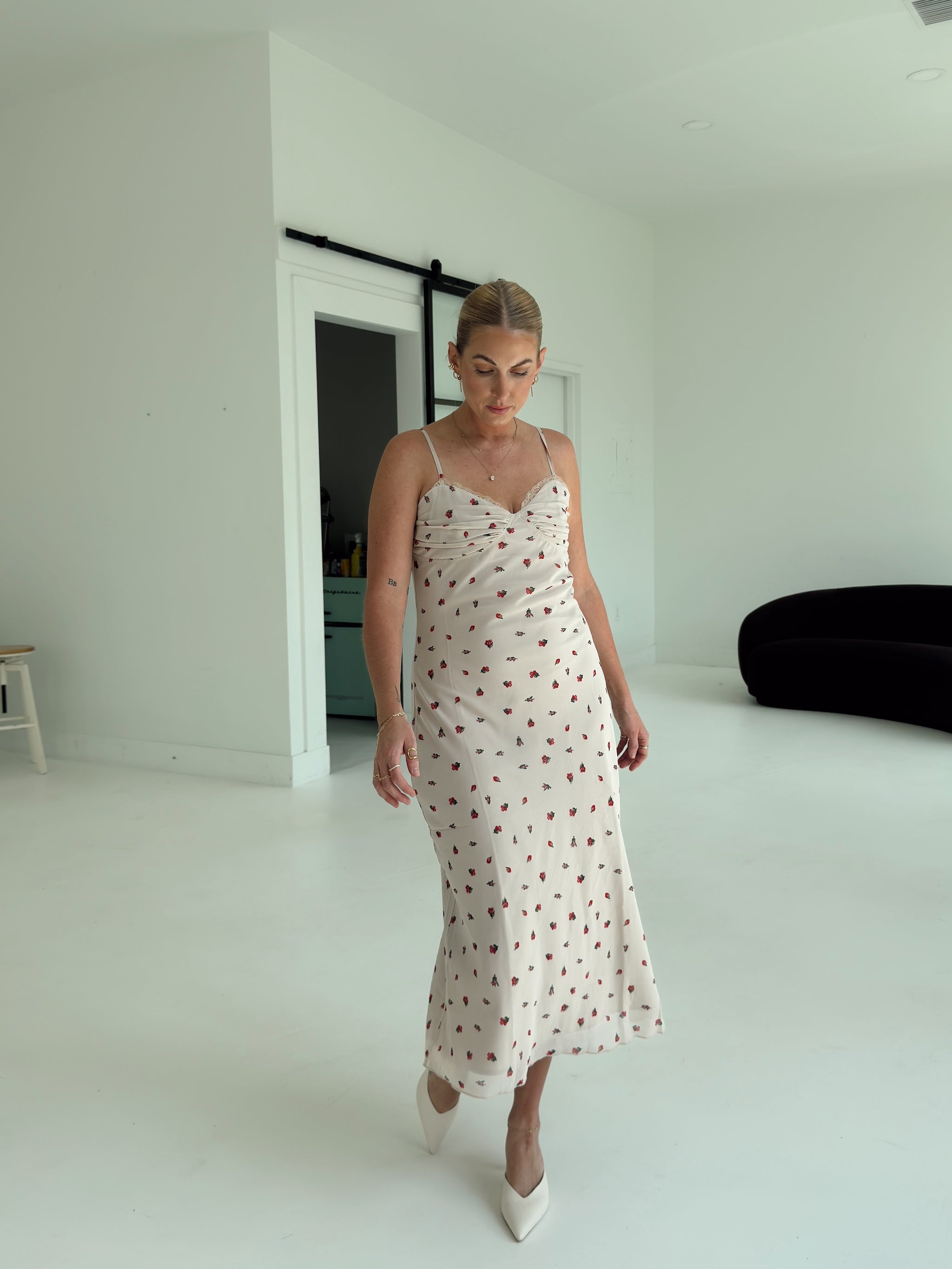 A model wearing a beige spaghetti-strap slip dress with small red ditsy floral print and lace trim.