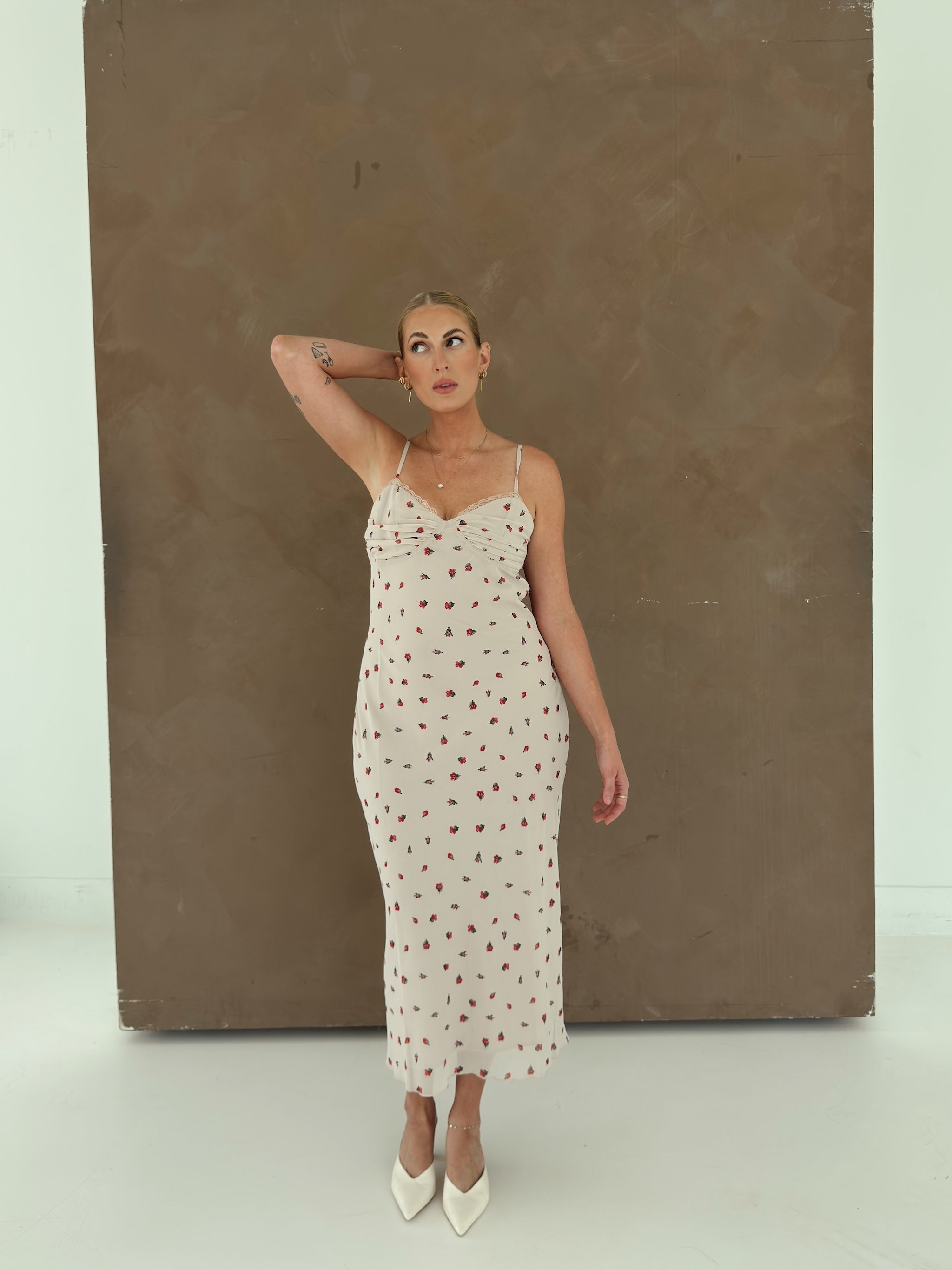 A model wearing a beige spaghetti-strap slip dress with small red ditsy floral print and lace trim.