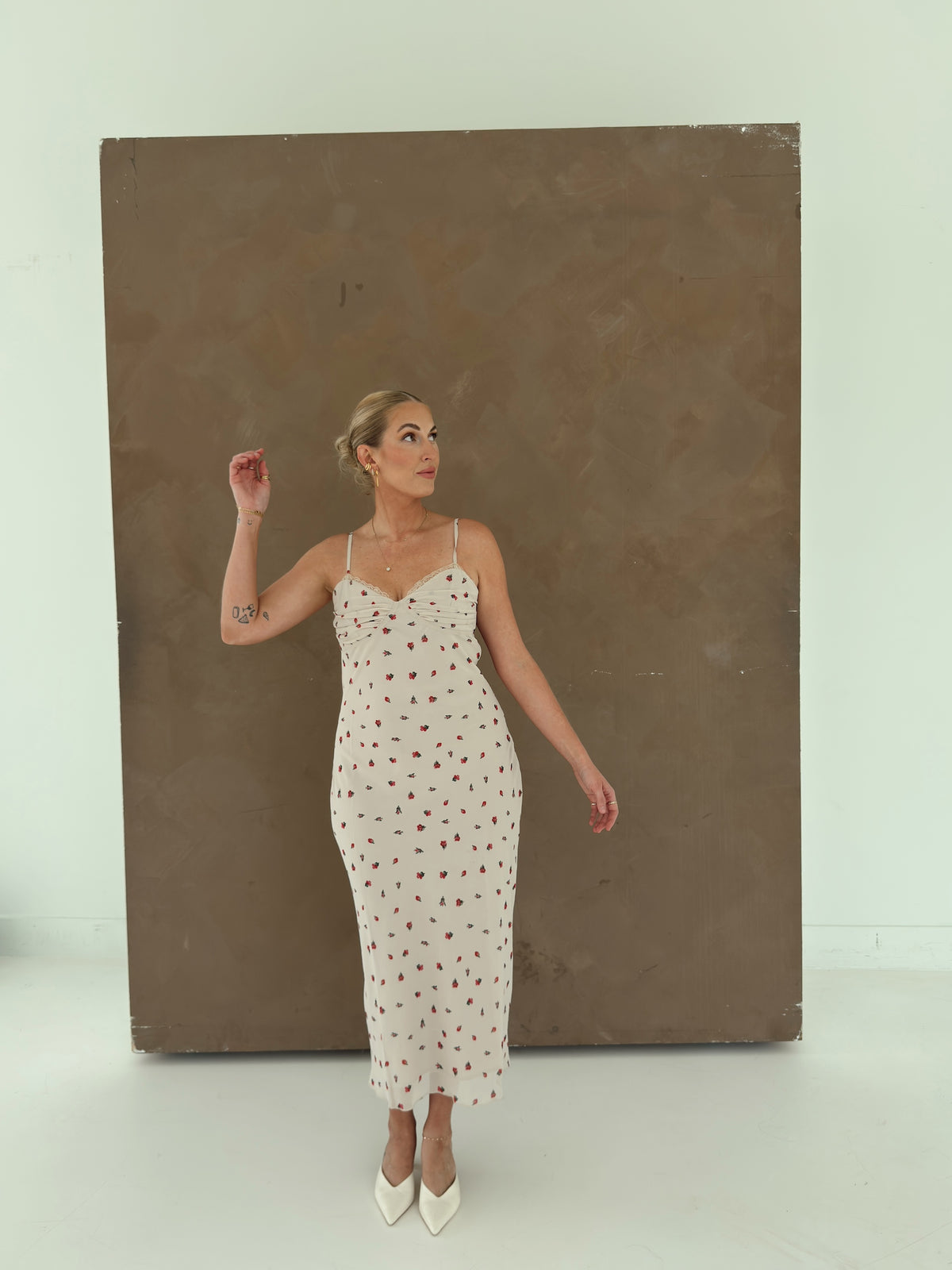 A model wearing a beige spaghetti-strap slip dress with small red ditsy floral print and lace trim.