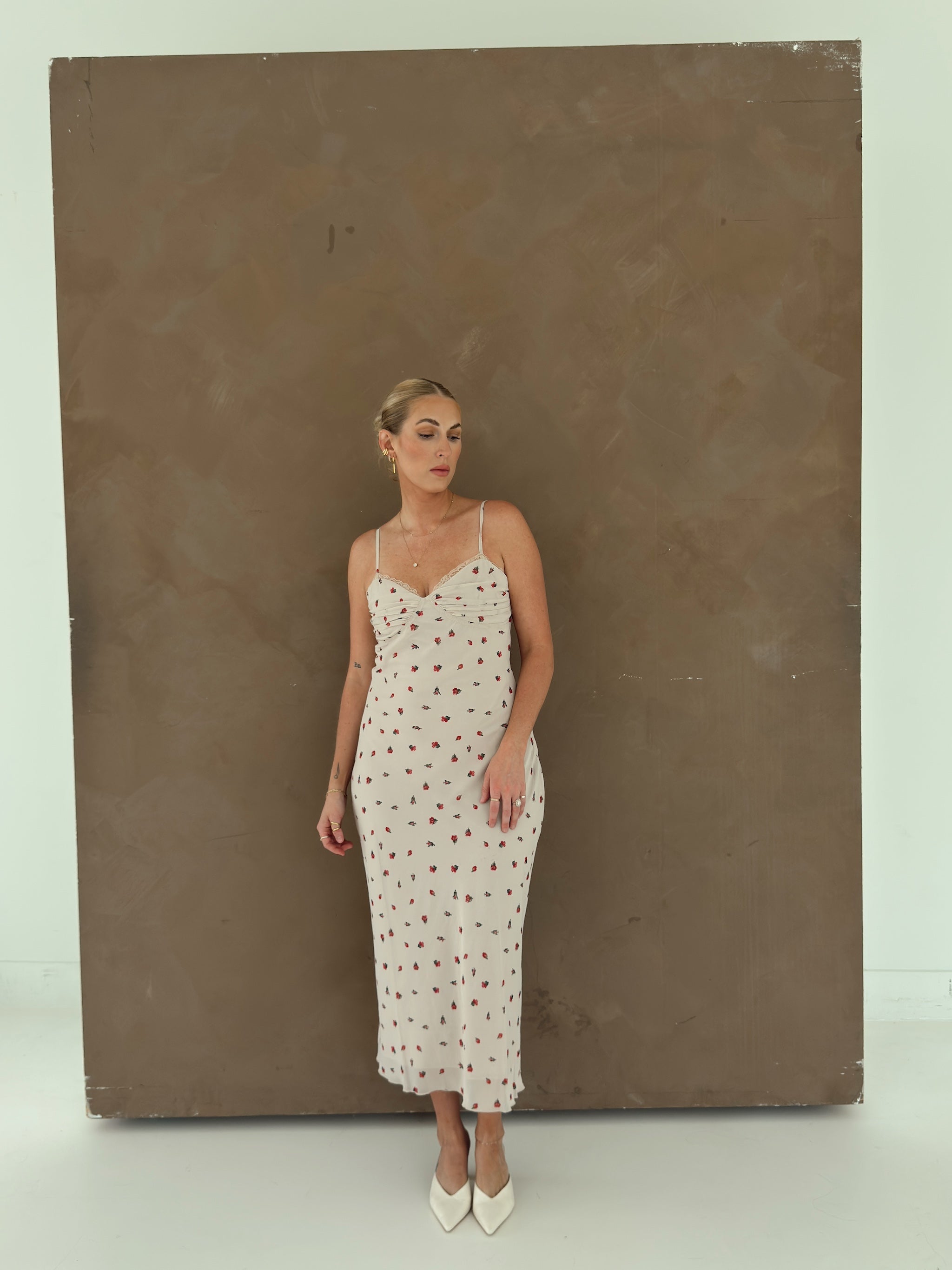 A model wearing a beige spaghetti-strap slip dress with small red ditsy floral print and lace trim.