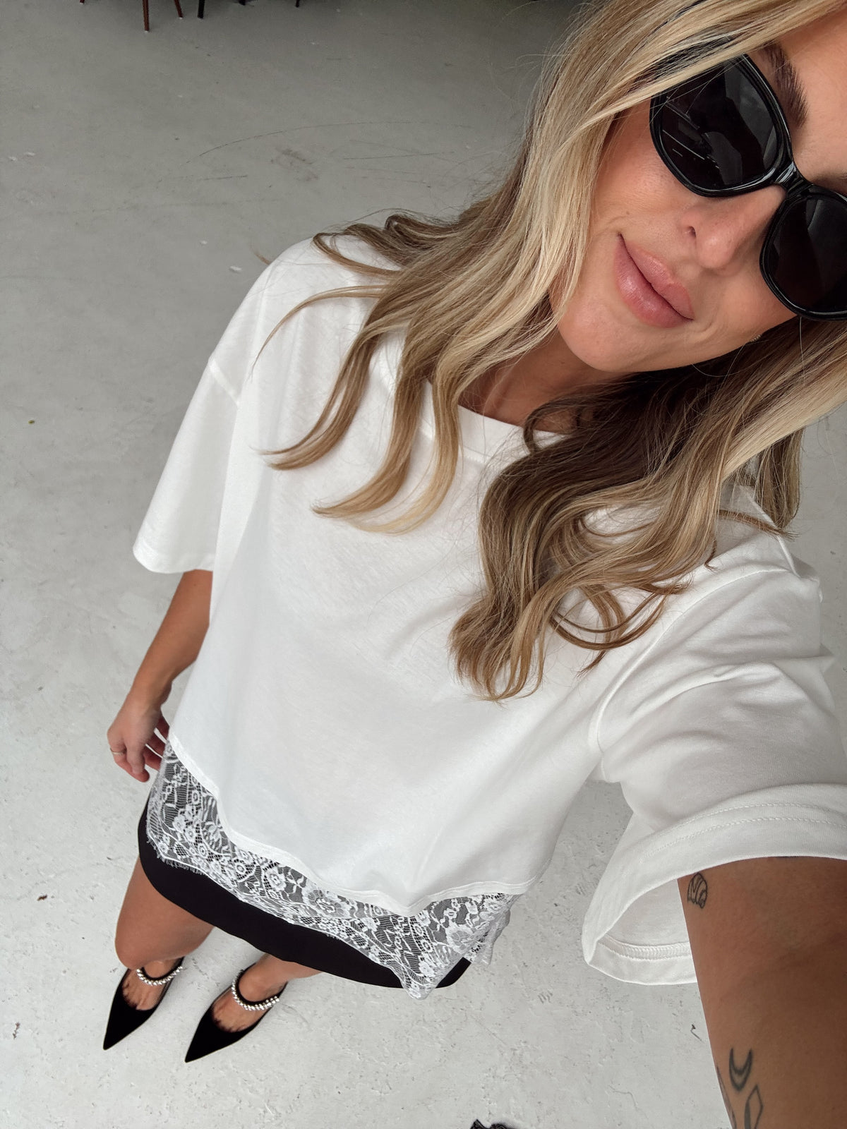 a woman in a white oversized t-shirt with a white lace hem paired with a black skort  and pointed toe heels 