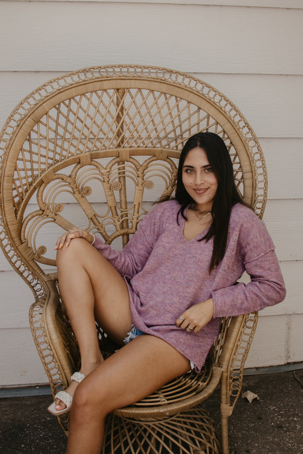 Female model wearing a rainbow fleck sweater and relaxing in a chair.